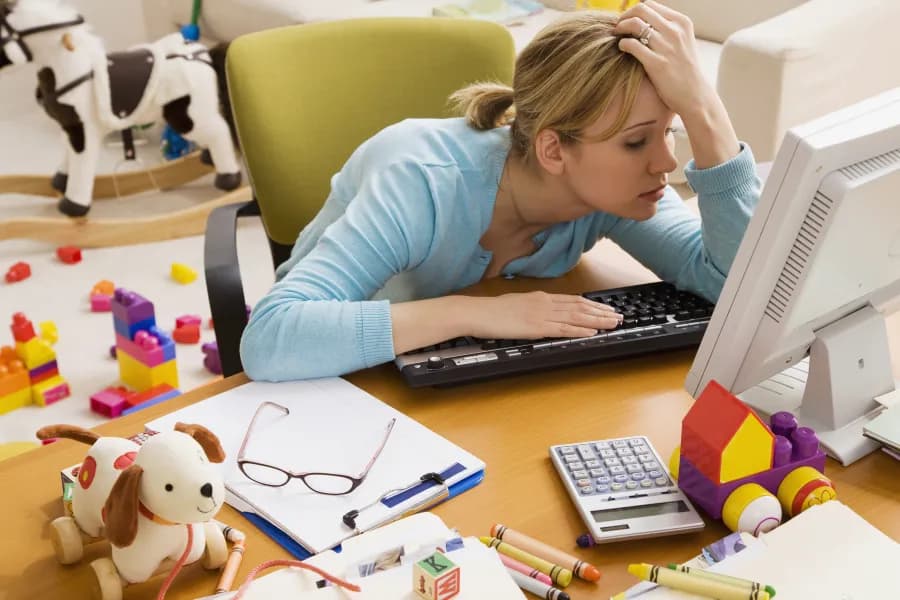 Mère fatiguée devant son ordinateur, jouets d’enfants autour